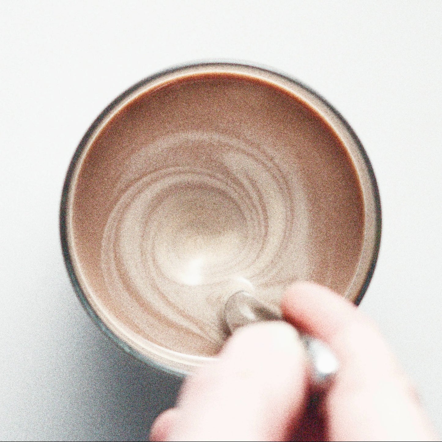 Close-up of a hand holding a mug with a swirling pattern of Cocoa Metro Belgian Instant Chocolate Drink Mix with milk in a cup on a white background.