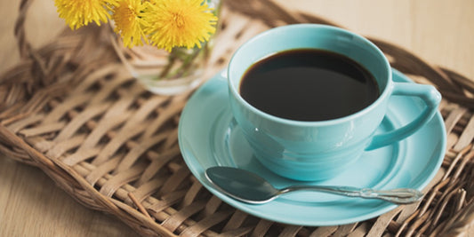 A turquoise cup and saucer featuring an inviting cup of coffee placed upon a rattan tray with daffodils in the background. 