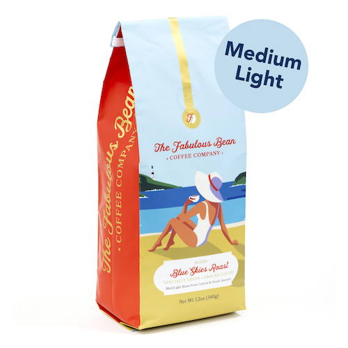 Fabulous Bean Coffee's Blue Skies Medium Light Ground Roast in a 12 ounce bag featuring a sophisticated woman enjoying coffee on a beautiful beach