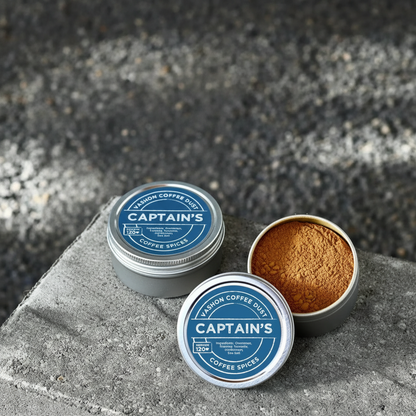 Two full size tins of Captain's flavor coffee dust from Vashon Island on a stone surface.  The label indicates 120 servings.