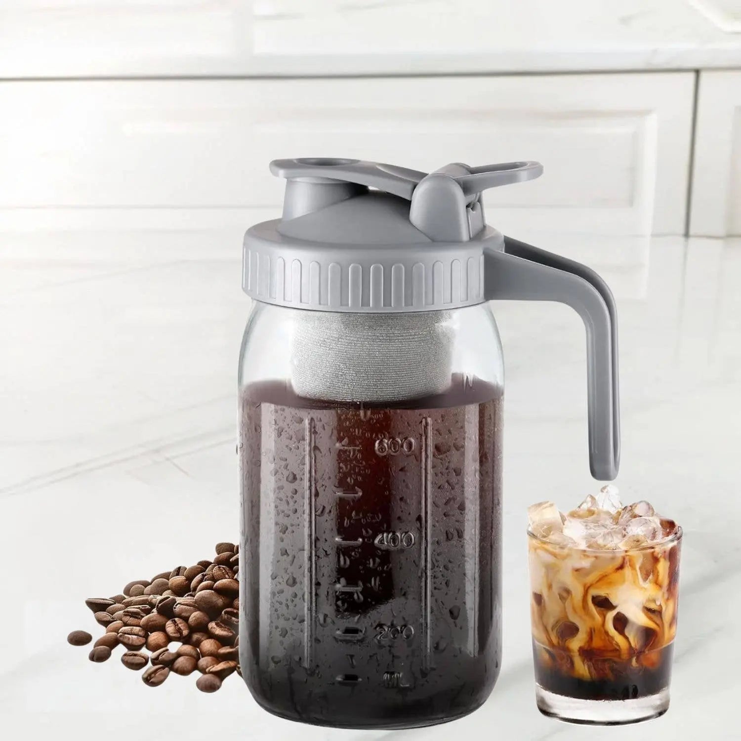 Cold Brew Coffee Maker in 32 oz by Zulay depicted against a white background with a handful of coffee beans and a cold brew coffee in a glass on either side. 