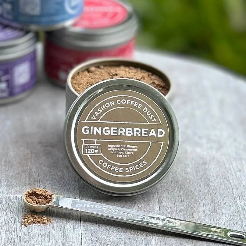Vashon Island Gingerbread flavor coffee spice mix in full-size tin with a measuring spoon alongside it on a wooden surface.