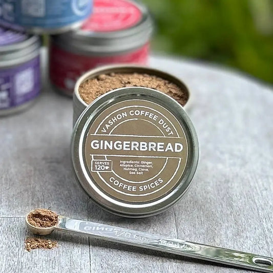 Vashon Island Gingerbread flavor coffee spice mix in full-size tin with a measuring spoon alongside it on a wooden surface.