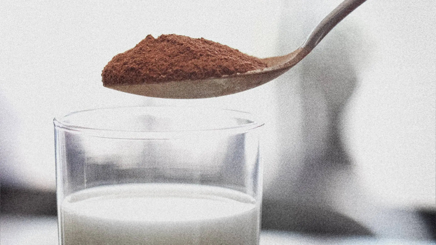 Spoonful of Cocoa Metro Instant Belgian Chocolate drink mix over a glass of milk on a white background.