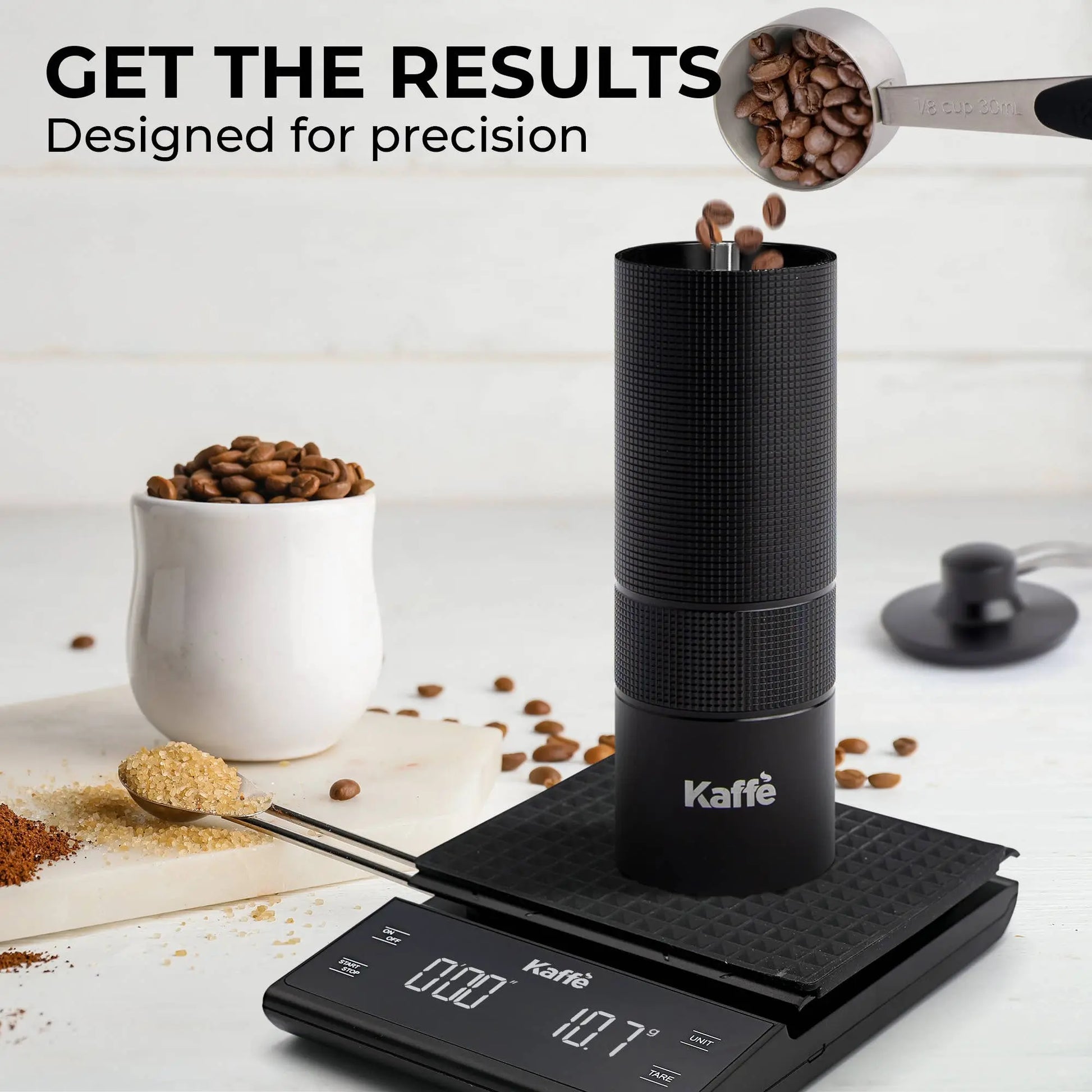 Manual coffee grinder by Kaffè is depicted atop a digital scale as coffee beans are being placed inside the grinder.