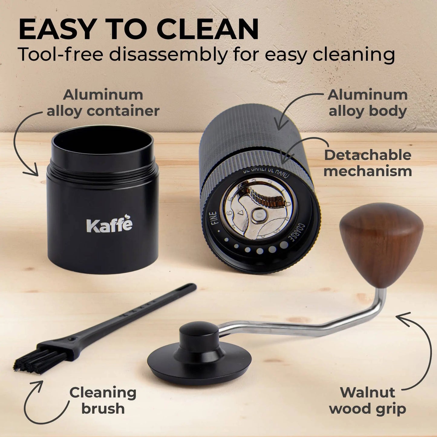 Kaffe coffee grinder with detachable mechanism, cleaning brush, and wooden handle on a wooden surface.
