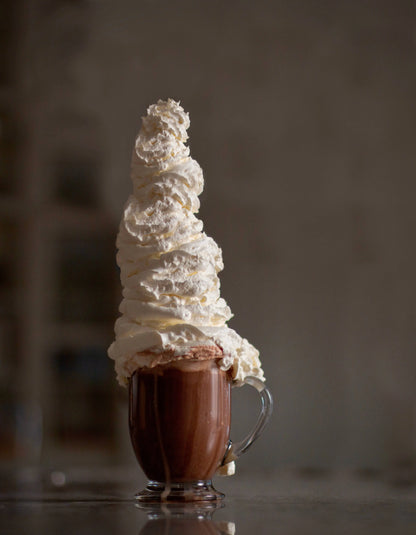 Hot chocolate with a tall tower of whipped cream made with Cocoa Metro Organic Belgian Chocolate mix on a dark background.