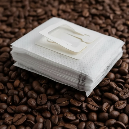 Stack of white single serve coffee filters on a bed of coffee beans.