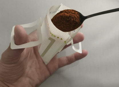 Demonstration of holding open a single serve coffee filter and adding coffee to it with a teaspoon.