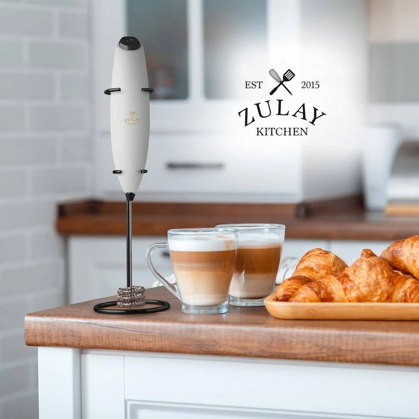 Zulay Kitchen milk frother with two coffee cups and croissants on a kitchen counter.